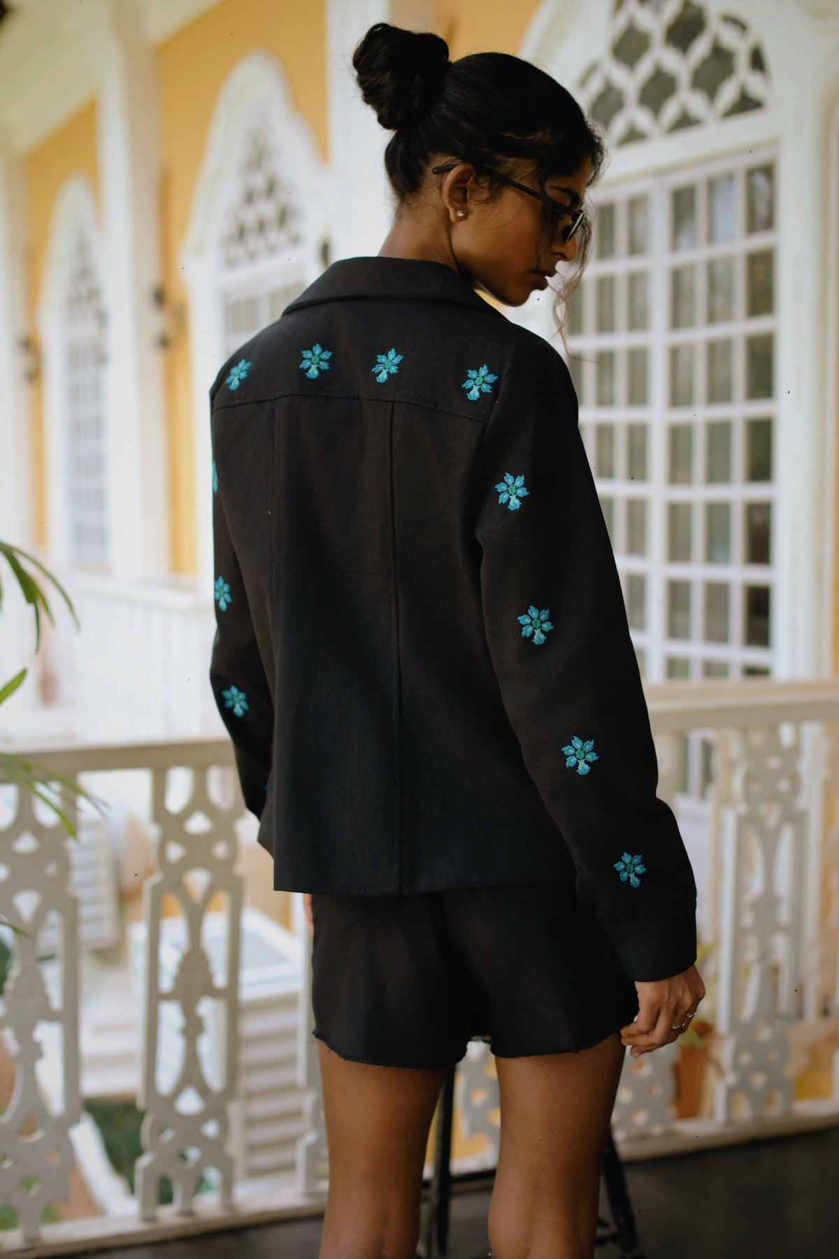 Back image of model wearing black embroidered jacket with blue floral embroidery
