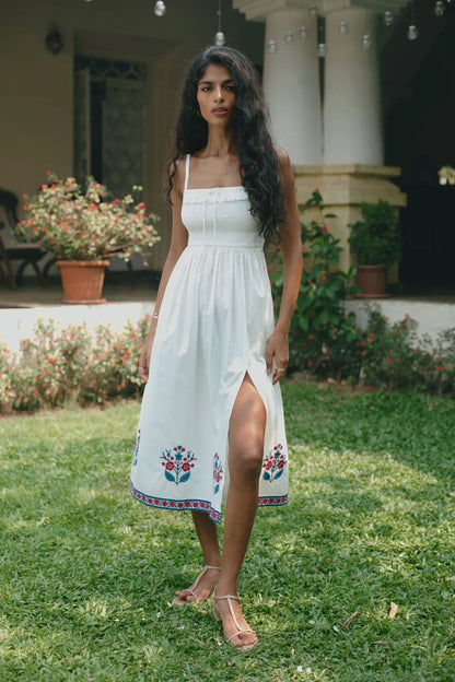 Front view of white cotton poplin fit-and-flare midi dress with red and blue floral embroidery, a smocked bodice, slit on the leg and adjustable straps— Amaya World