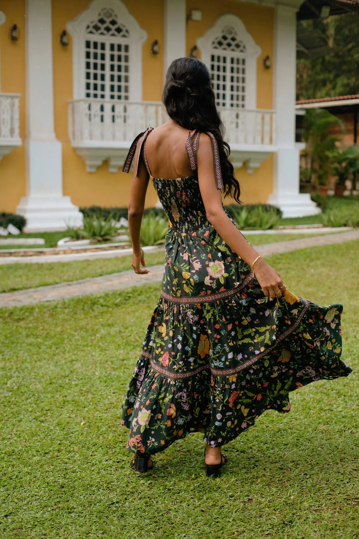 Back view of Black floral tiered cotton maxi sundress with tie-up straps and fit-and-flare silhouette — Black wedding guest dress - Amaya World