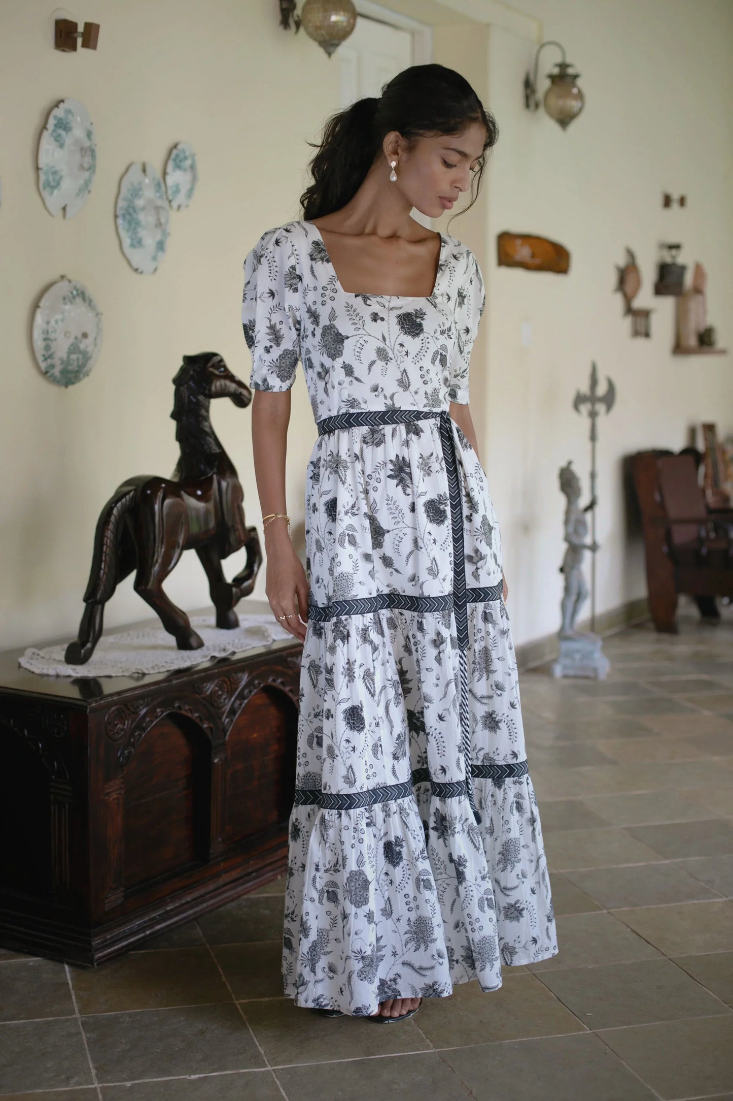Front view of boho style tiered maxi dress with floral print in white and black with square neckline, puff sleeves and boho style tiered silhouette showcasing the full length of the maxi dress and styling  — Amaya World