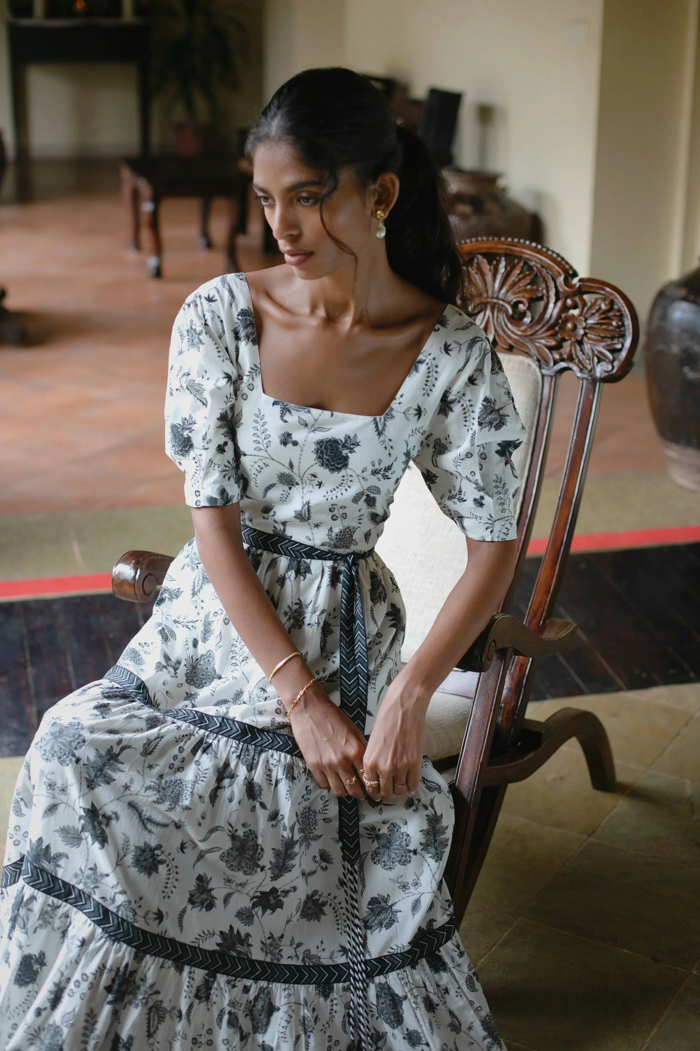 Mid length view of white maxi dress with square neckline and puff sleeves. This floral boho maxi dress showcases detail of the hand-painted floral print, and tie-up belt attached at the waist  — Amaya World