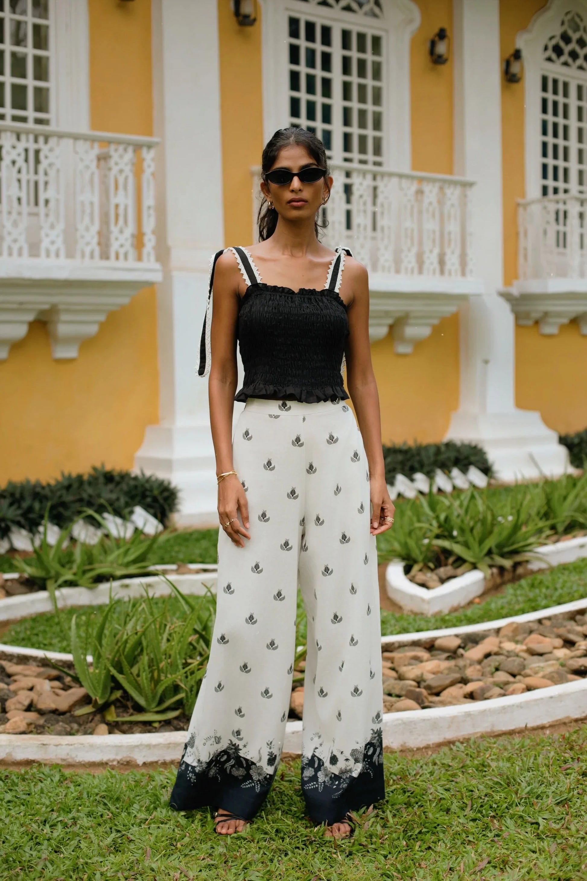 Front view of black and white floral print high-waisted wide-leg cotton linen blend trousers styled with black crop top with smocking and lace detail - Amaya World