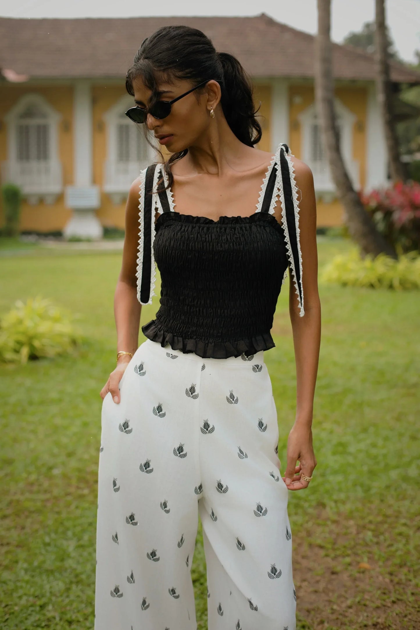 Close-up of black and white floral print high-waisted wide-leg cotton linen blend trousers styled with black crop top with smocking and lace detail on tie-up straps - Amaya World