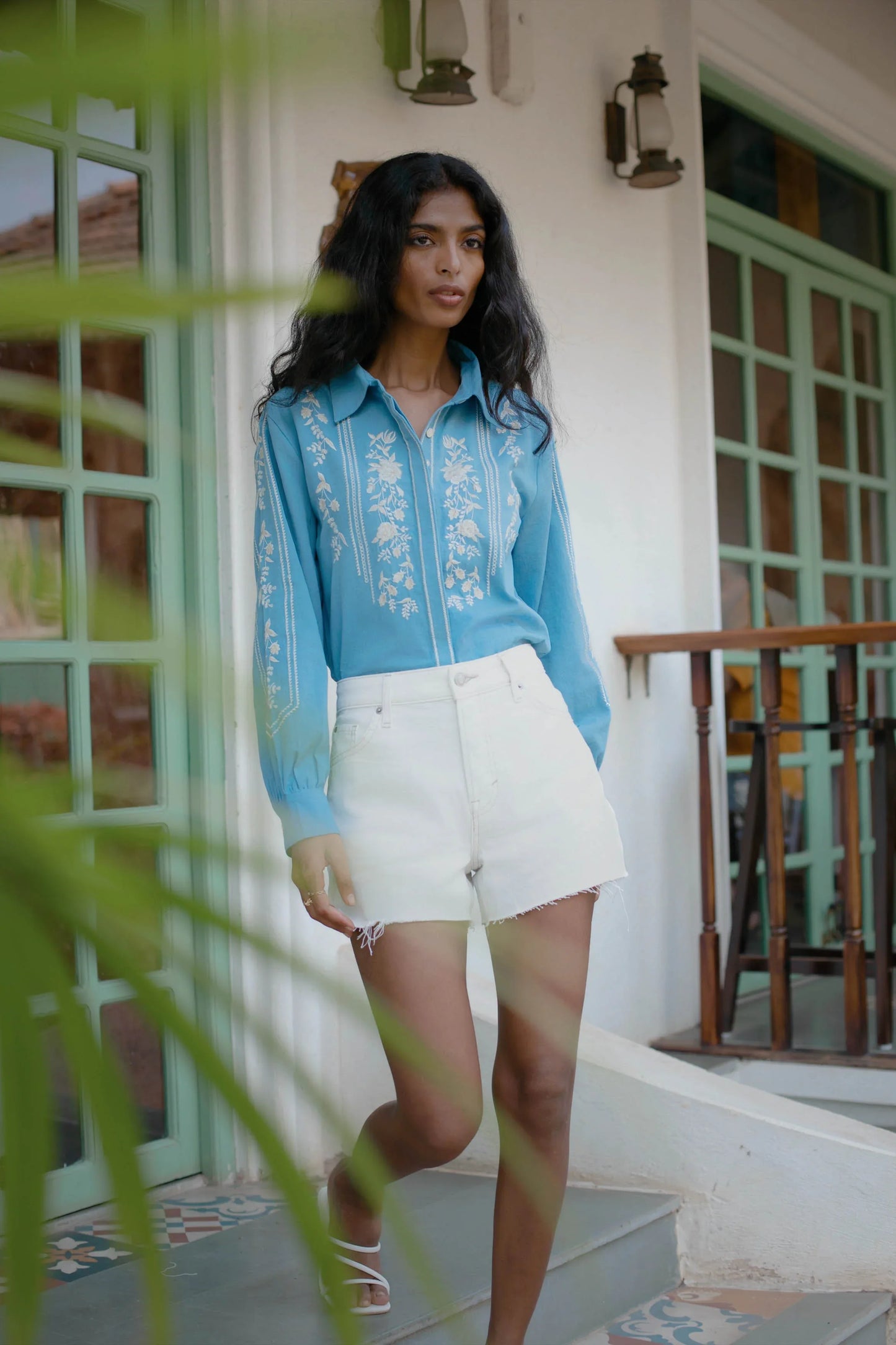 Blue embroidered cotton shirt with collar, full sleeves and cuffed hems styled with white shorts — Amaya World artisan blouse