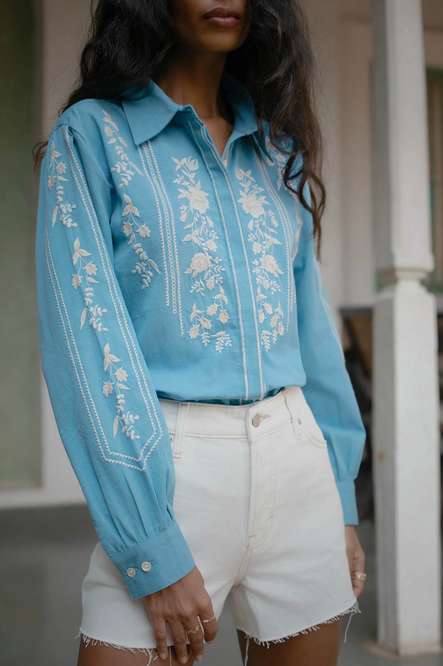Close-up of white thread floral embroidery on blue cotton button-down shirt with focus on the embroidery on sleeves— Amaya World slow fashion