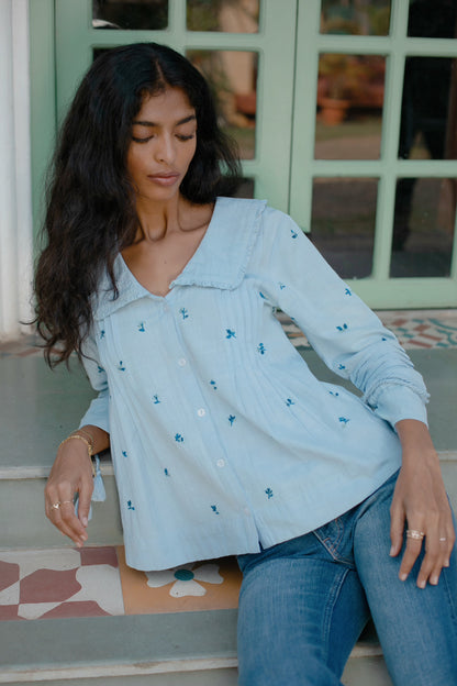Close-up of light blue hand-embroidered cotton linen boho blouse with oversized frill collar and tassel sleeves —| Amaya World